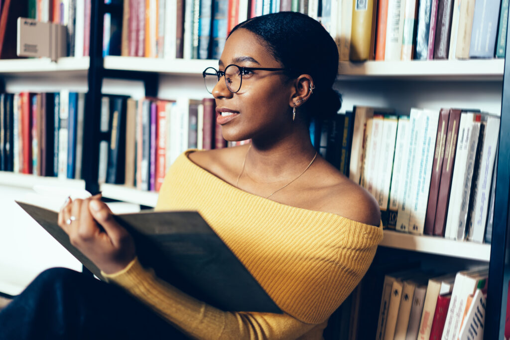 Smart student reading book beside bookcase